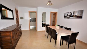 A dining area with a wooden table and chairs, a kitchen in the background, and a painting on the wall. - Apartament Suiza - Calafell (Calafell)