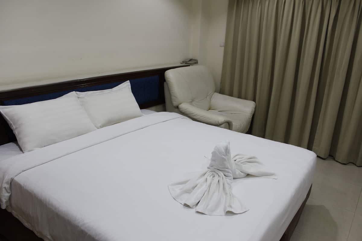Une chambre d’hôtel avec un lit bien fait, une chaise et un rideau.