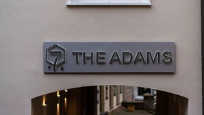 A sign for "The Adams" hotel with a geometric logo and a simple, modern design. - THE ADAMS- Self Check in Hotel (Baden-Baden)