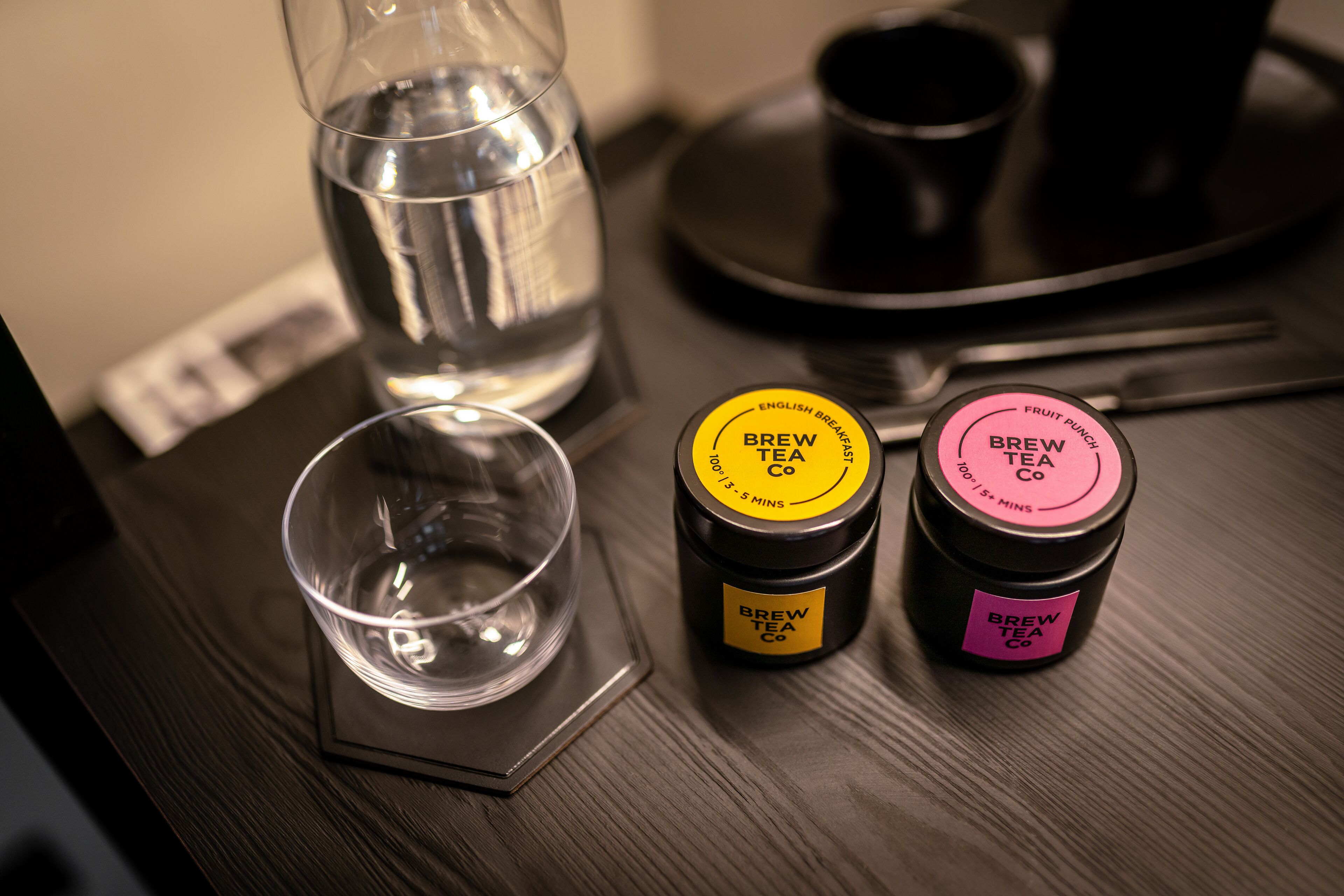 A table with a glass of water, a tea cup, and two containers of Brew Tea Co. tea.
