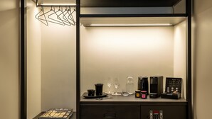 A compact, dark-colored room with a built-in desk, a small refrigerator, and a shelf with a book and a towel. - THE ADAMS- Self Check in Hotel (Baden-Baden)