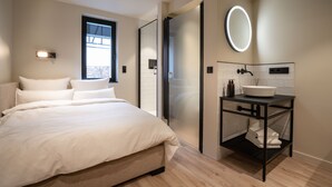 A modern bedroom with a large bed, a bedside table with a white basin, and a wall-mounted mirror. - THE ADAMS- Self Check in Hotel (Baden-Baden)