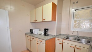 A compact kitchen with a microwave, toaster, and coffee maker on the countertop, a sink, and cabinets with wooden handles. - Apartment Lindamar - Calafell (Calafell)