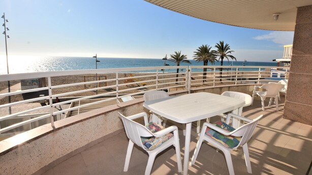 A terrace with a table and chairs, overlooking a beach with palm trees and the sea. - Apartment Lindamar - Calafell (Calafell)