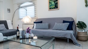 A modern living room with a grey sofa, striped pillows, a glass coffee table, and a painting on the wall.