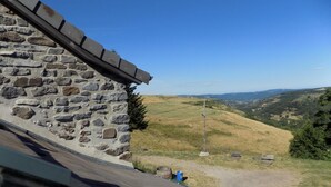 Een stenen gebouw met een schuin dak, met uitzicht op een glooiend landschap onder een heldere lucht.