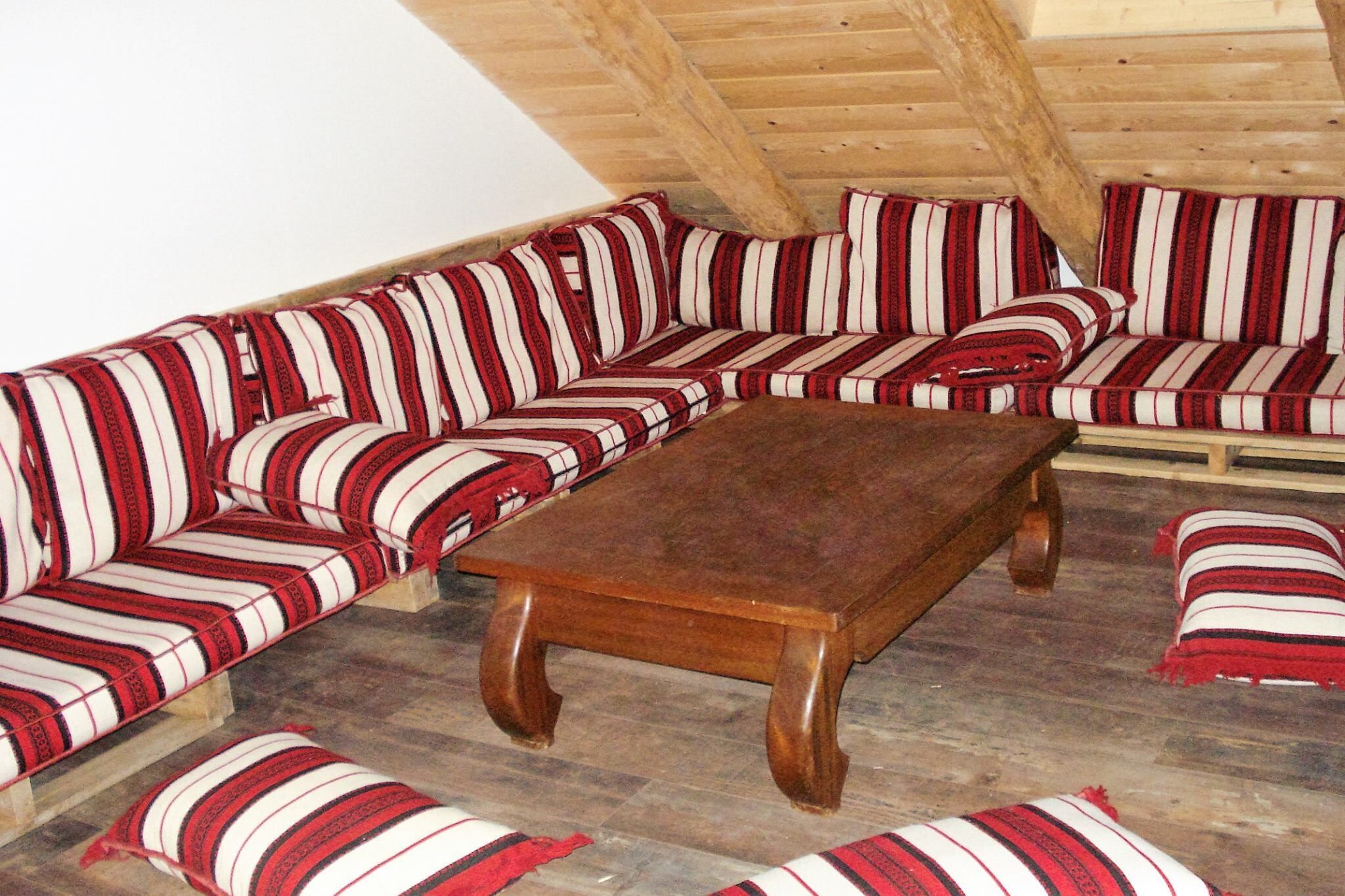 A wooden ceiling with exposed beams, a wooden table, and striped sofas with pillows.