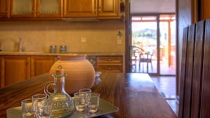 A wooden table with a pitcher and shot glasses, a vase, and a wooden bench in a kitchen with wooden cabinets and a view of the outdoors.