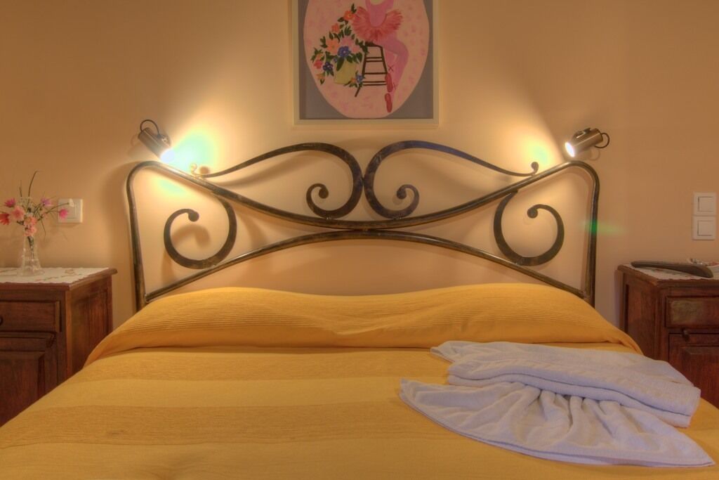 A bed with a metal headboard, a yellow bedspread, and a white towel on the bed.