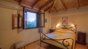 A bedroom with a wooden ceiling, a bed with a metal frame, a bedside table, and a window with a view of the outside.