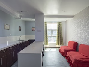 A modern kitchen with a central island, a dining area with red upholstered chairs, and a view of the outside through a window with green curtains. - OYO 549 Sajj Bldg (Baguio)