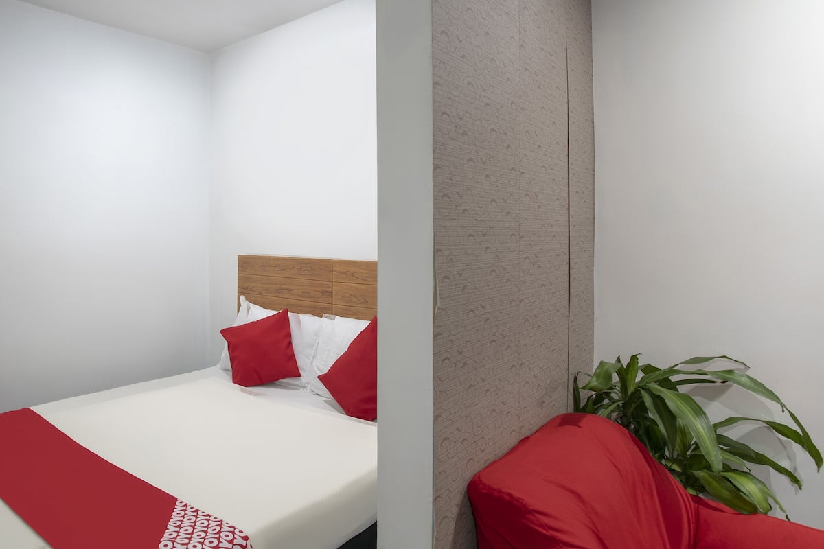 A modern bedroom with a wooden headboard, white bedding, red pillows, and a red throw blanket.