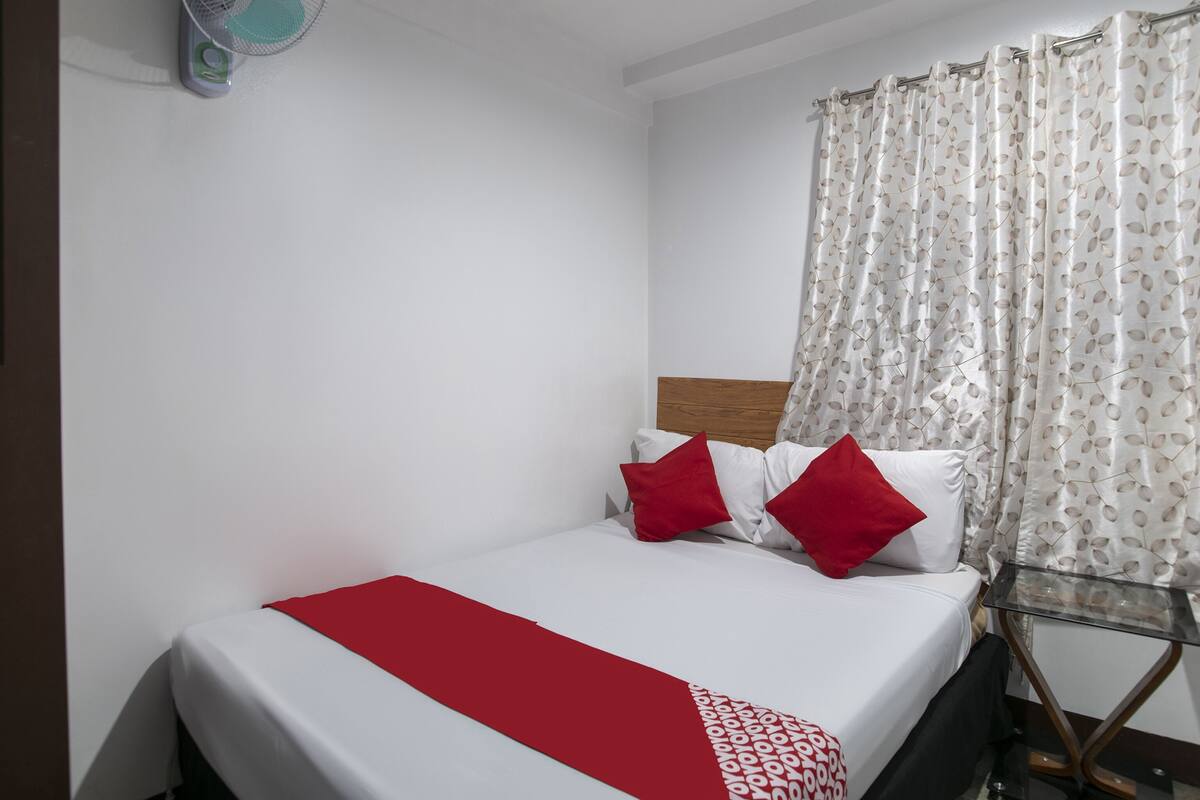 A hotel room with a bed, a fan, and a curtain.