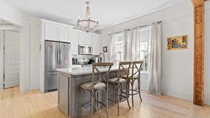 A modern kitchen with white cabinetry, stainless steel appliances, and a central island with bar stools. - Luxe 3BR on Magazine St with private pool & patio. Sleeps 6, walk to cafés, near FQ & Superdome. (New Orleans)