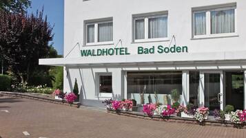 Ein Hotel namens Waldhotel Bad Soden mit heller Fassade, großen Fenstern und Blumenbeeten mit rosa und weißen Blüten.