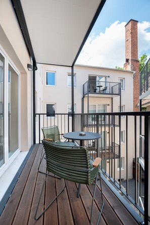 A balcony with a table and chairs, a view of a building with a brick chimney, and a clear sky. - Limehome Leipzig Jahnallee (Leipzig)