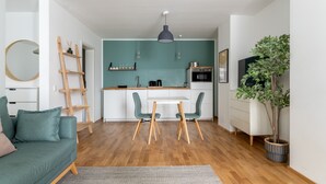 A modern kitchen with teal cabinets, a white countertop, and a dining area with a table and chairs. - Limehome Leipzig Jahnallee (Leipzig)