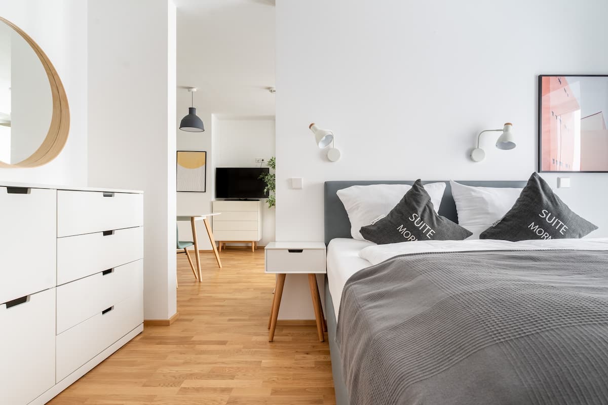 A modern hotel room with a bed, bedside tables, a desk, and a wardrobe.