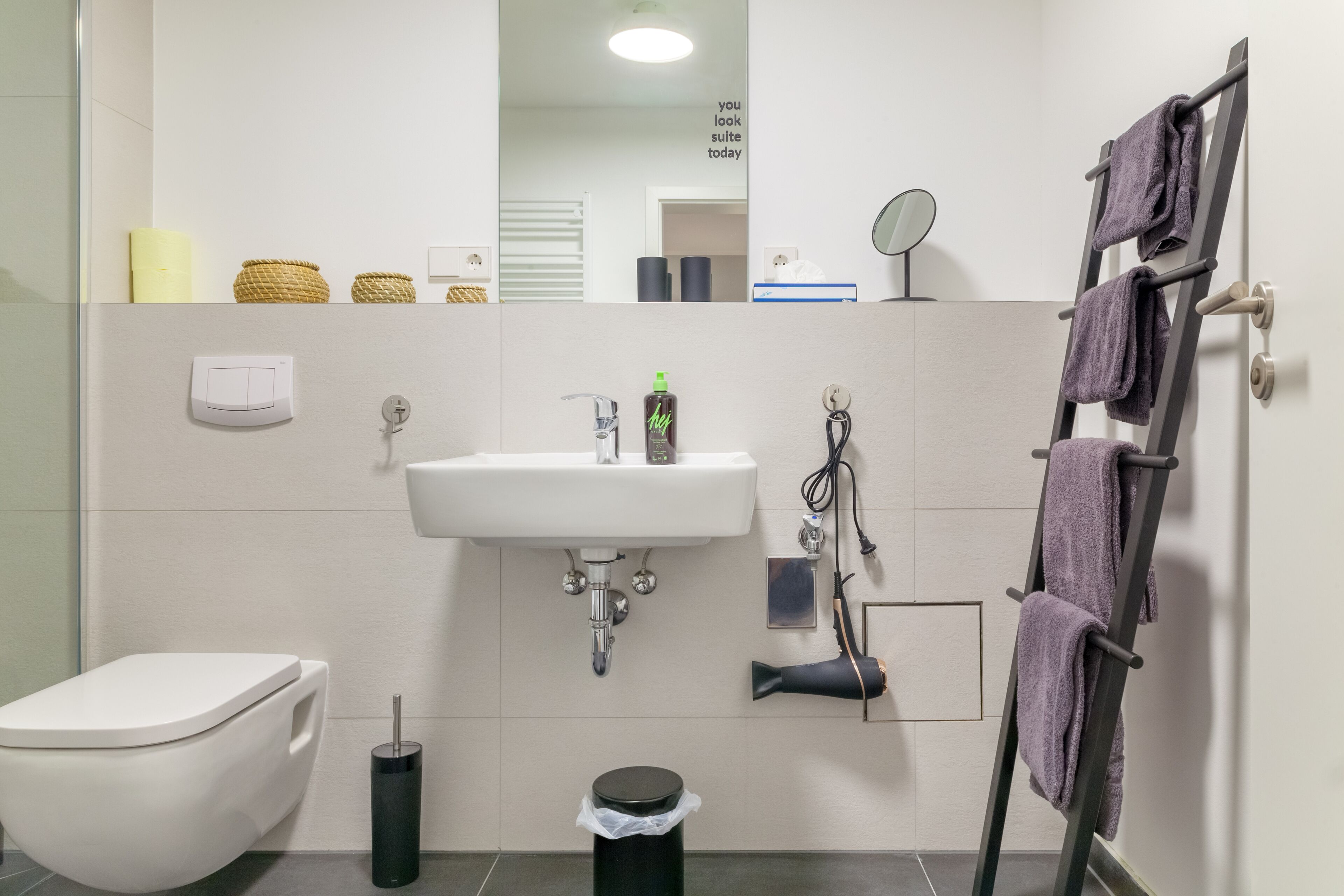 Ein Badezimmer mit weißem Waschbecken, Toilette, Mülleimer und Handtuchhalter mit Handtüchern.