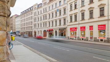 Eine Straße mit einer Straßenbahn, Gebäuden mit Beschilderung und einem Bürgersteig mit Mülleimer und Fahrrad.