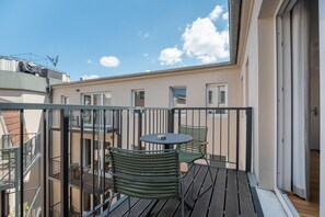 A balcony with a round table and two chairs, overlooking a building with multiple windows. - Limehome Leipzig Jahnallee (Leipzig)