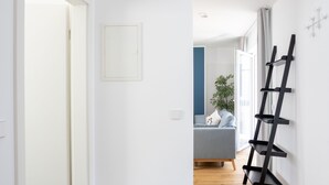 A hallway with a wooden floor, a white door, a white wall, and a black ladder leaning against the wall. - Limehome Leipzig Jahnallee (Leipzig)