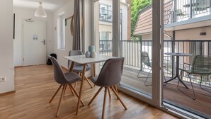 A modern apartment with a dining area featuring a table and chairs, large windows with a view of the neighborhood, and a balcony with outdoor furniture. - Limehome Leipzig Jahnallee (Leipzig)