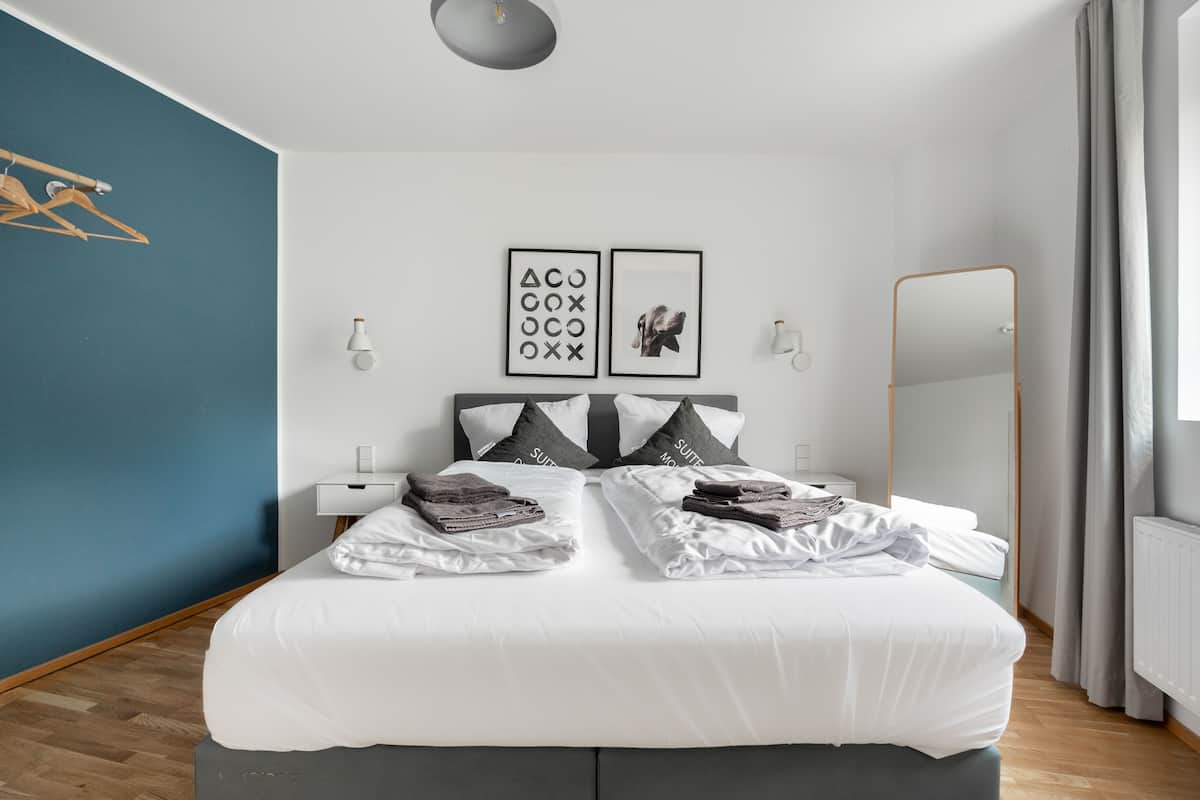 A modern bedroom with a large bed, two bedside tables, a mirror, and wall art.