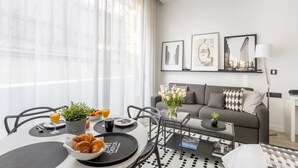 Un salon moderne avec un coin repas, comprenant un canapé, une table basse et une table à manger dressée avec des croissants et du jus d’orange.