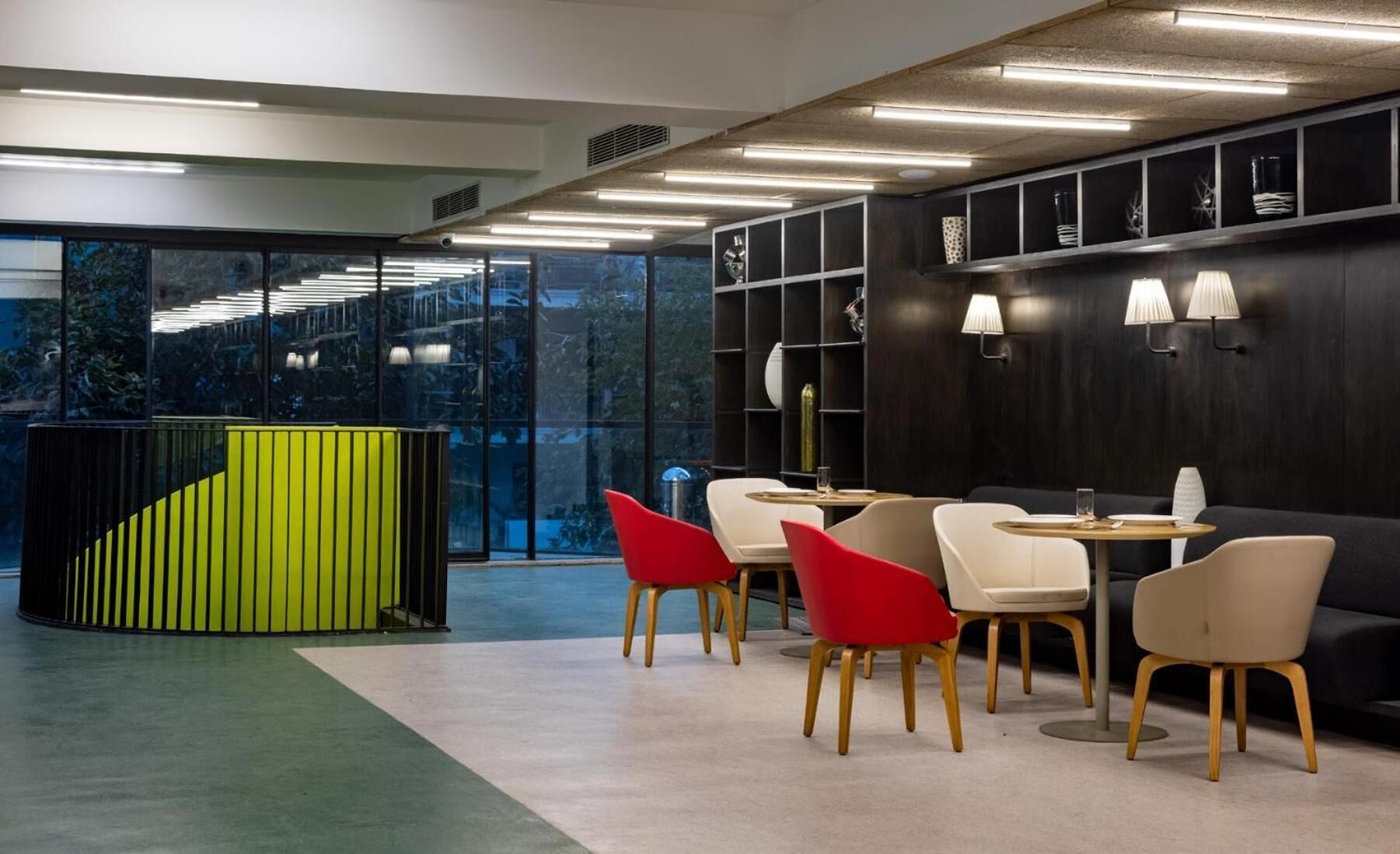 Een modern interieur met een groene accentmuur, een zwart wandrek en een zithoek met rode en witte stoelen.