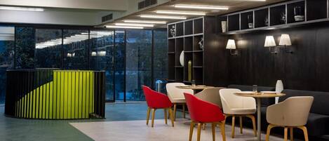 Een modern interieur met een groene accentmuur, een zwart wandrek en een zithoek met rode en witte stoelen.
