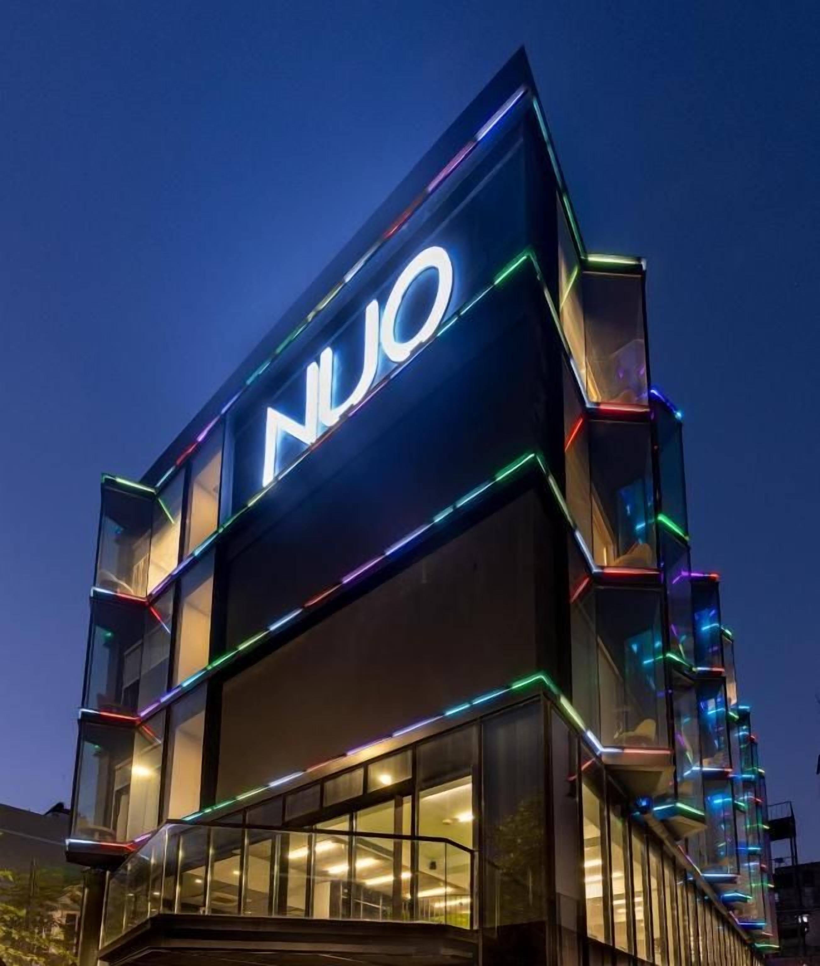 A modern building with a prominent 'NUO' sign, featuring a glass facade and illuminated edges.