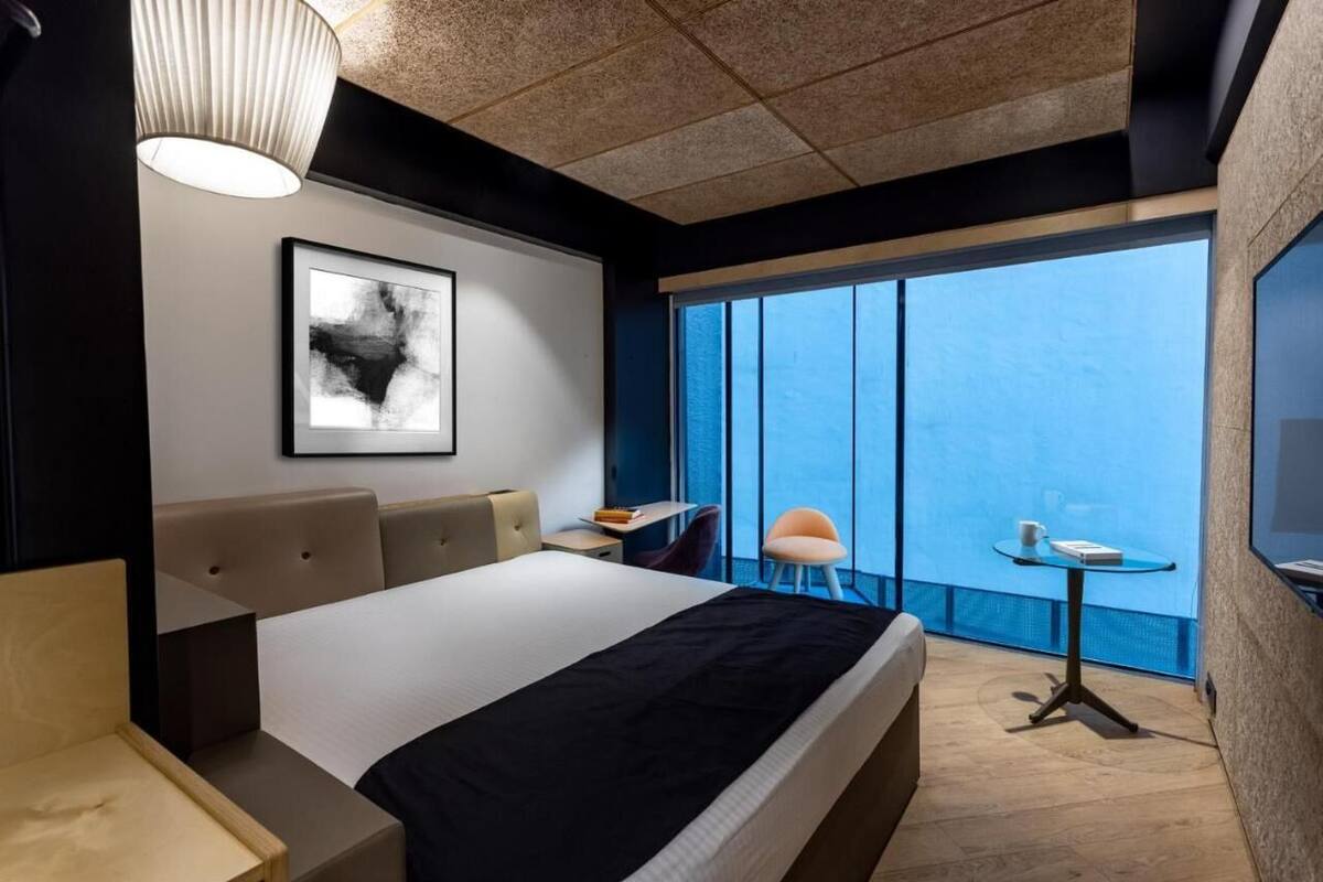 Habitación de hotel moderna con una cama grande, un escritorio, una silla, una mesita y un ventanal con vistas.