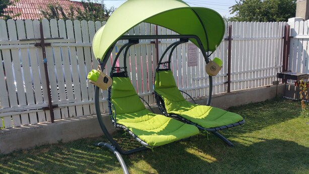A green outdoor chair with a canopy, attached to a metal frame, positioned on grass near a white picket fence. - Vila 21A (Costinesti)