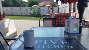 A patio area with a table labeled "FIVE KITCHEN," outdoor seating, and a white picket fence in the background. - Vila 21A (Costinesti)