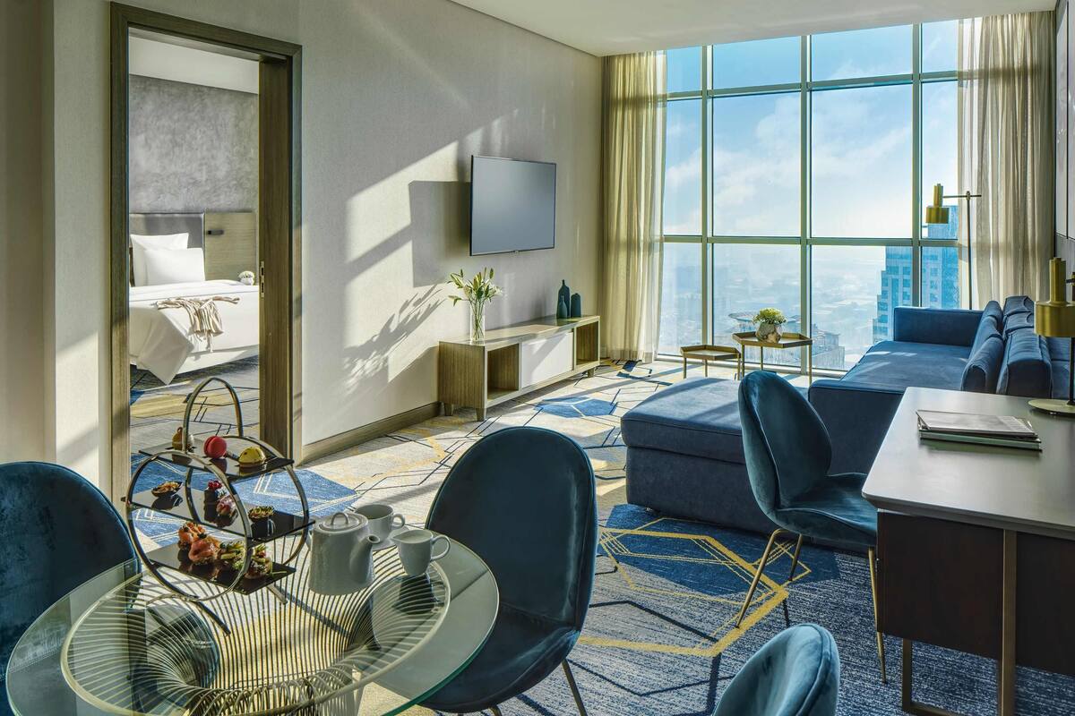 A modern hotel room with a large bed, a sofa, a dining area, and a TV.