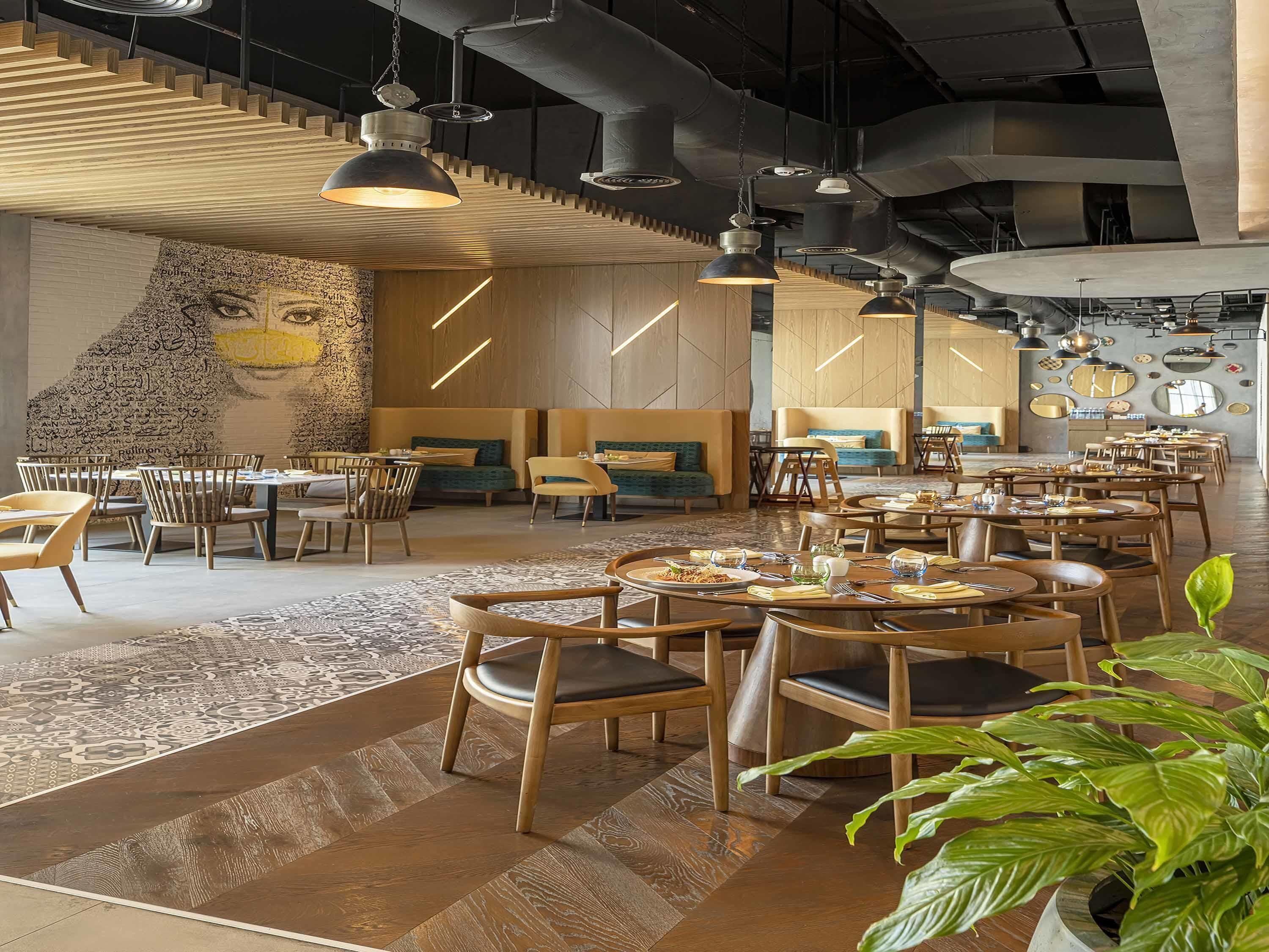 Un restaurante moderno con mobiliario de madera, lámparas colgantes y un mural grande en la pared.