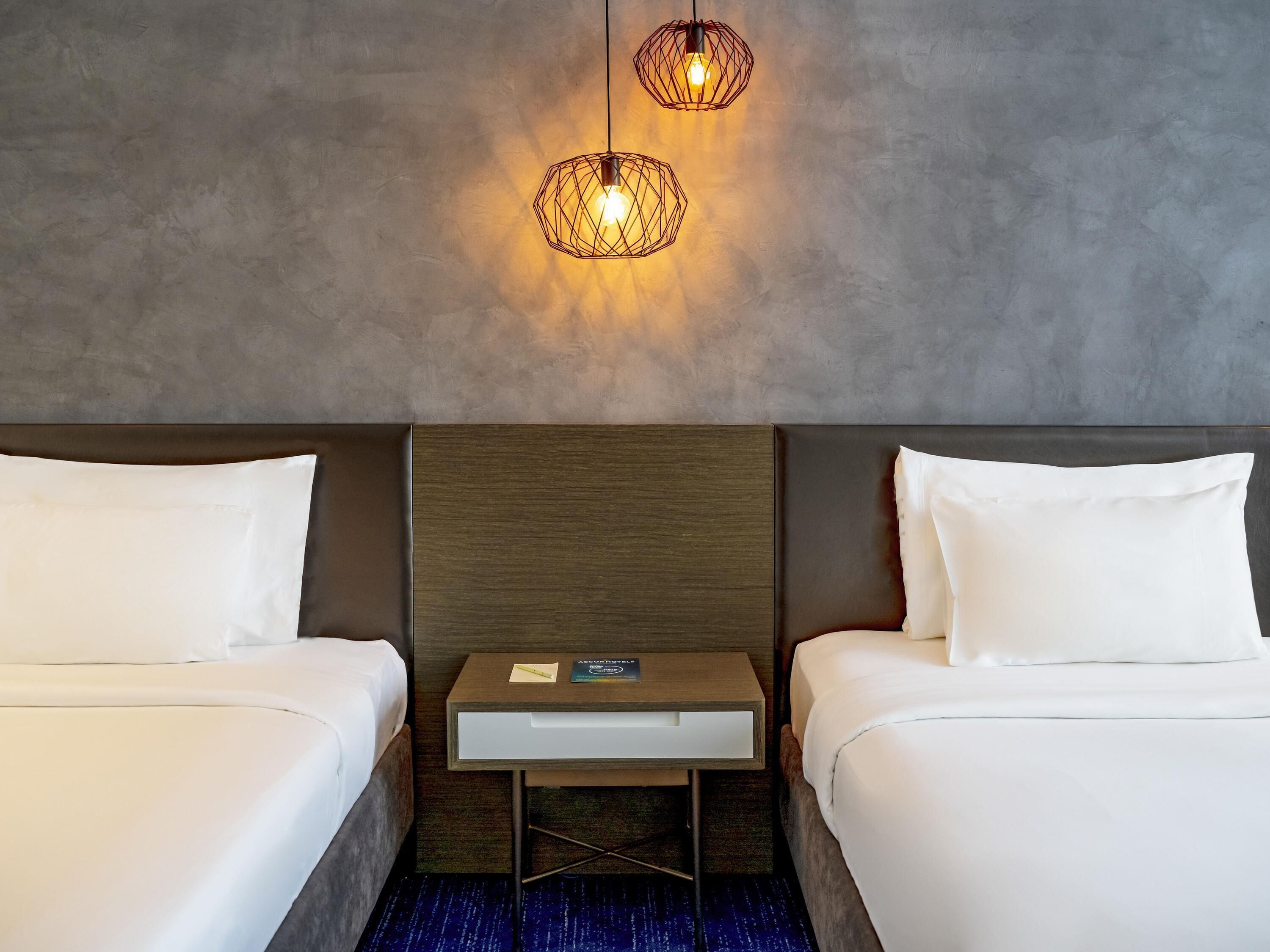 Une chambre d’hôtel avec deux lits, une table de chevet et deux lampes fixées au mur.