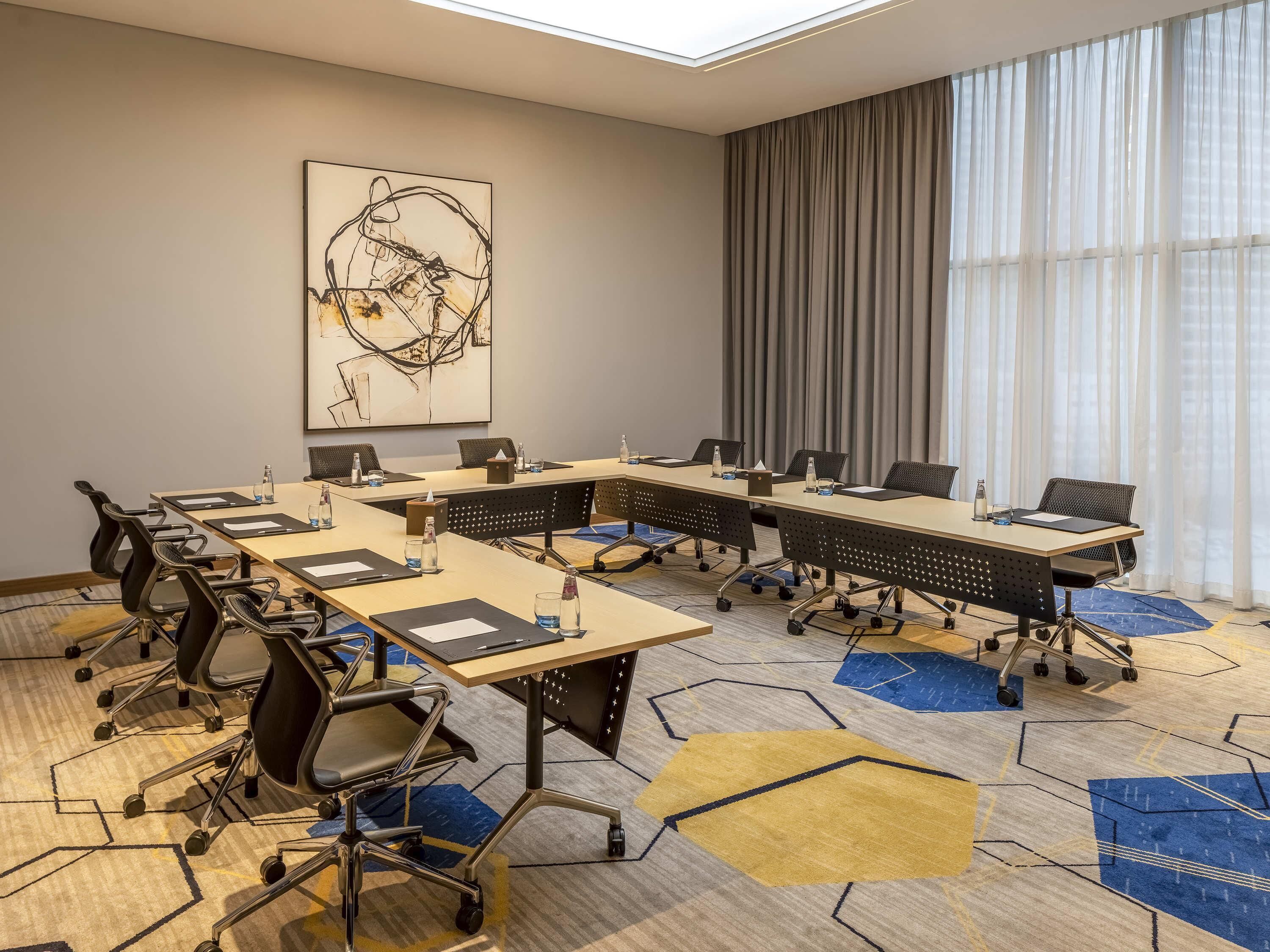 Une salle de conférence avec une grande table, des chaises et un tableau accroché au mur.