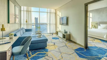 A hotel room with a large window, a sofa, a desk, a chair, a bed, and a TV.