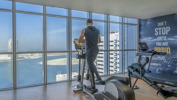 Un gimnasio con amplios ventanales que ofrecen vistas a un paisaje urbano y al agua.