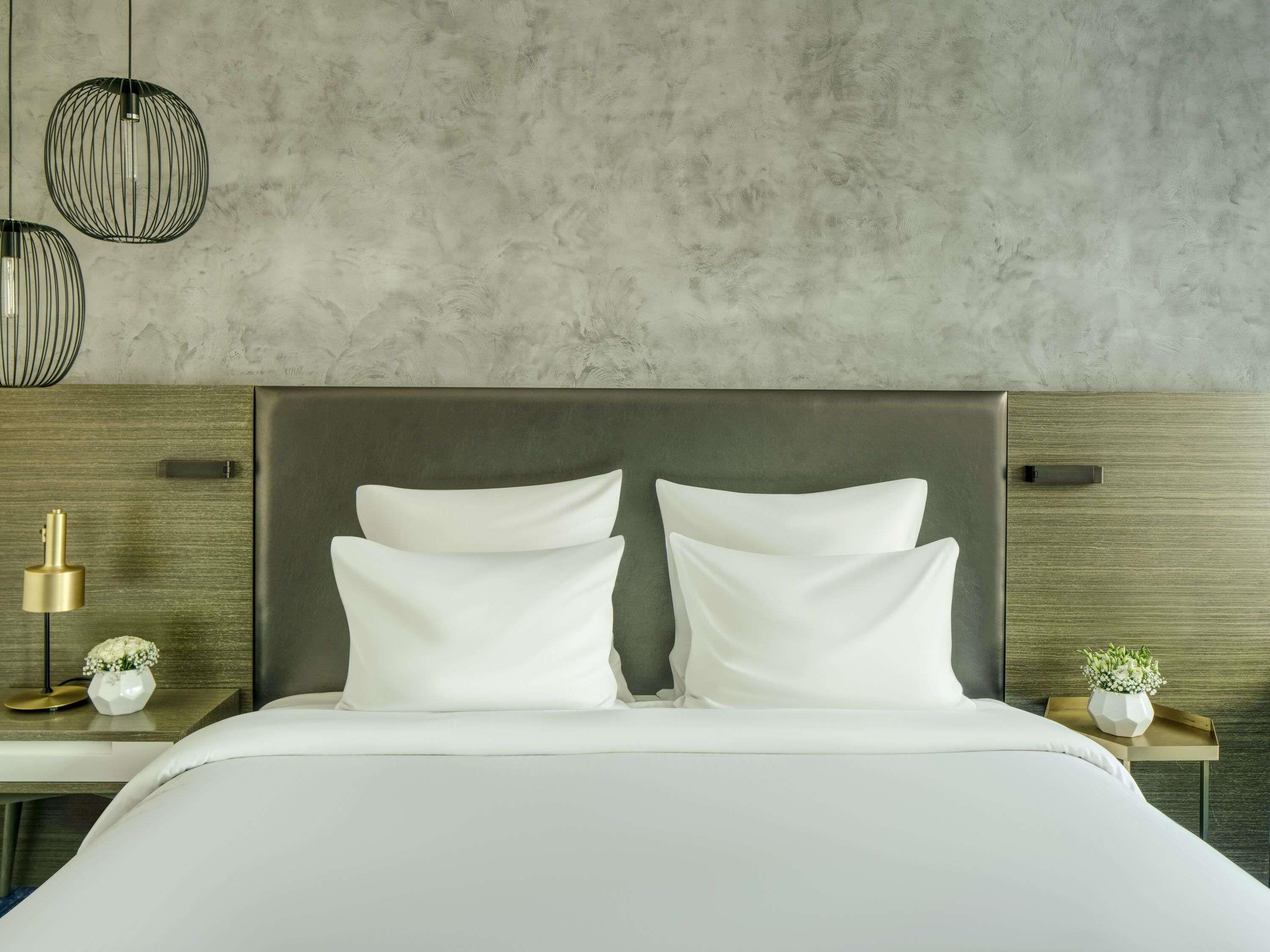 A modern bedroom with a large bed, two bedside tables, a wall-mounted light fixture, and a textured wall.