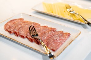 A plate of sliced salami with a fork and knife on a white table. - Aparthotel Adagio Leicester (Leicester)