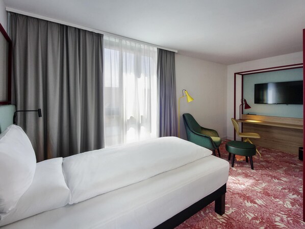 A hotel room with a bed, a desk, a chair, a TV, and a window with curtains. - ibis Styles Klagenfurt am Woerthersee (Klagenfurt am Woerthersee)