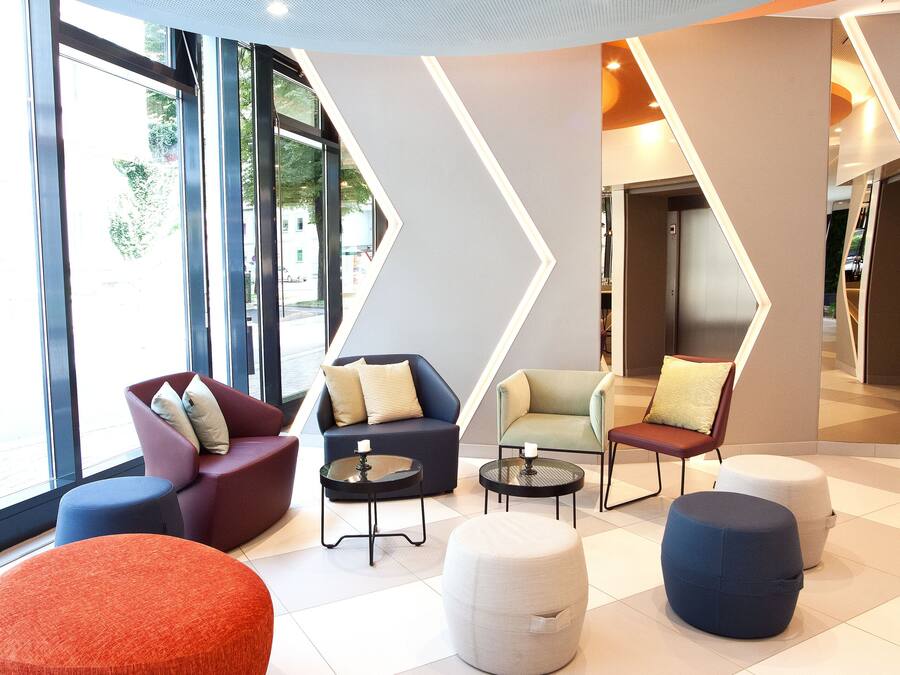 A modern lounge area with seating arrangements, large windows, and a geometric wall design.