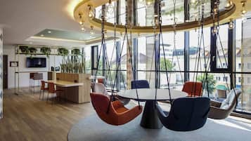 A modern interior with a central round table, hanging chairs, a TV, and large windows.