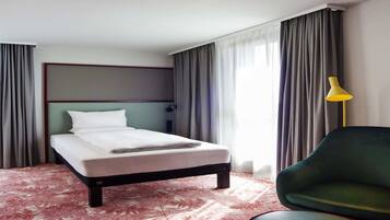 A hotel room with a bed, a chair, a lamp, and curtains.