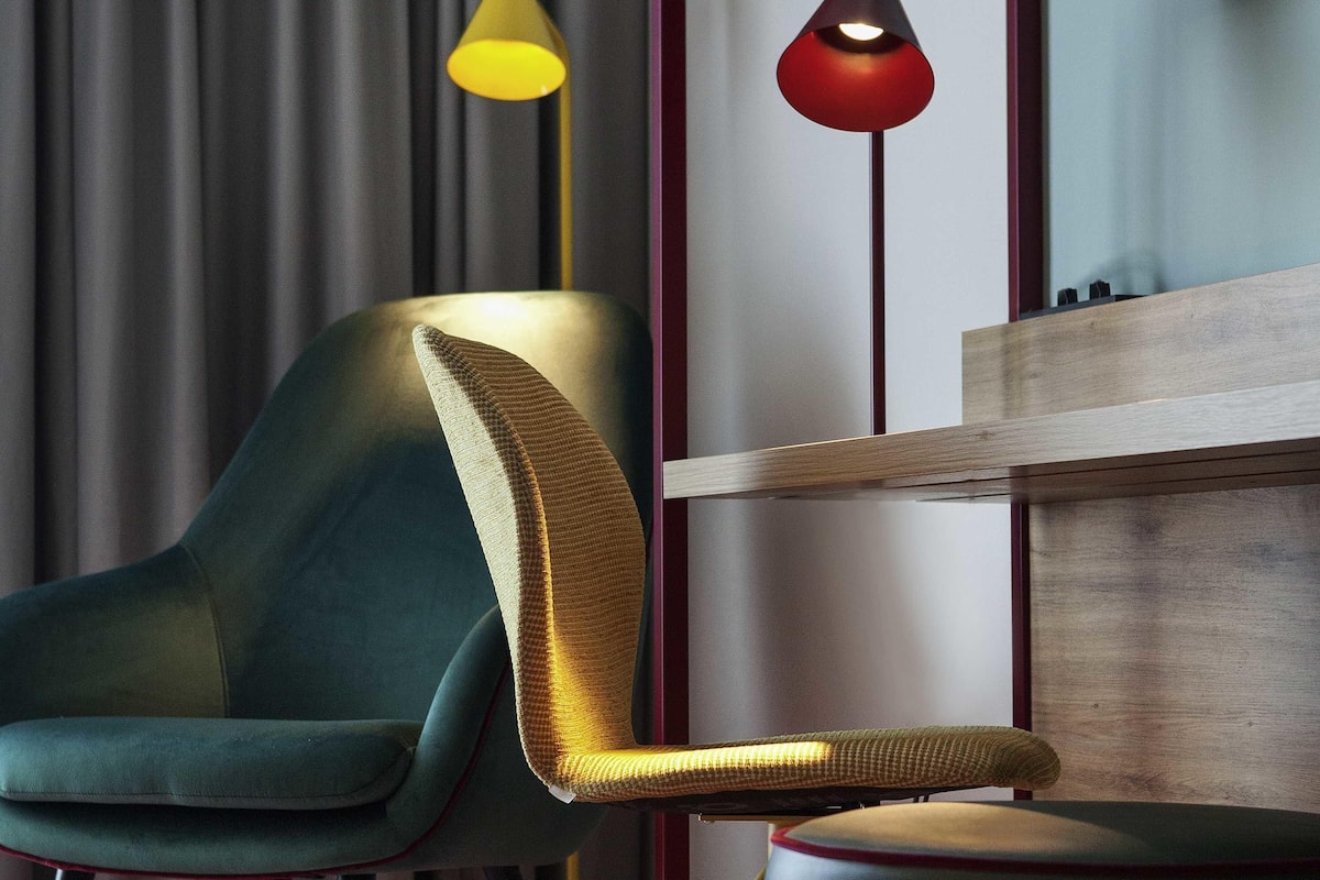 Une chaise moderne dotée d’accoudoirs texturés et d’un coussin, placée près d’un panneau en bois et d’un rideau.