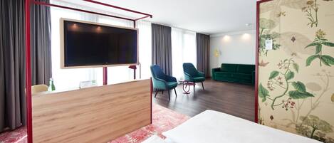 Habitación de hotel con una cama grande, un escritorio con televisor de pantalla plana, dos sillas, un sofá y un papel tapiz con motivos florales.