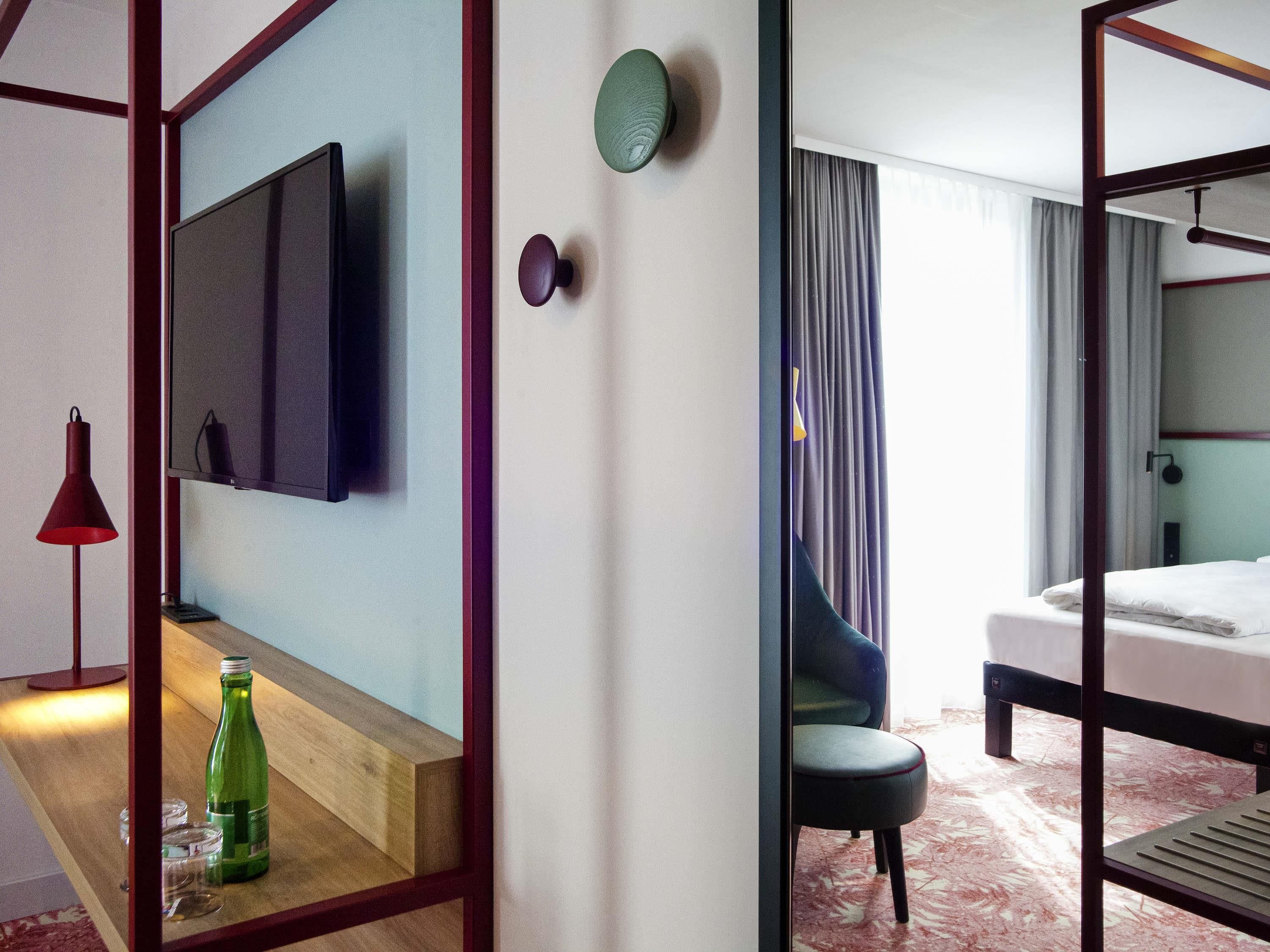 Hotelkamer met een bed, een aan de muur bevestigde televisie, een nachtkastje met een fles en glazen, en een stoel.